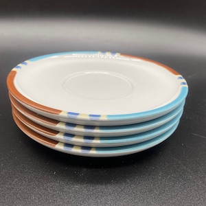 以下が含まれることがあります： 青と茶色の縁取りが施された白いセラミック製のソーサーが4枚。ソーサーは重ねられています。