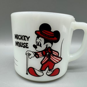 Op de afbeelding: Witte keramische mok met een zwart-rode illustratie van Mickey Mouse met een rode hoed en een stok. De tekst "Mickey Mouse" is in zwart op de mok gedrukt.