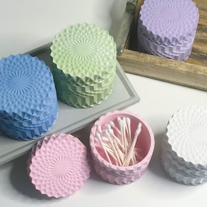 May include: Five decorative containers with a geometric pattern. The containers are in shades of blue, green, pink, and white. One container is filled with cotton swabs.