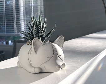 May include: A white ceramic planter shaped like a sleeping dog, with a small green succulent plant inside.