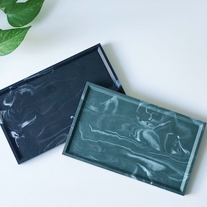 Peut inclure: Deux plateaux rectangulaires avec un motif marbré. Un plateau est noir avec un marbrage blanc, et l'autre est vert avec un marbrage blanc.