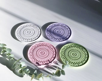 Puede incluir: Cuatro posavasos redondos con un diseño de mandala. Los posavasos son en tonos de morado, rosa, verde y blanco.