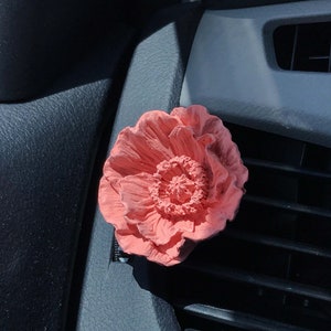 May include: A pink flower-shaped car air freshener hanging from a car's air vent.