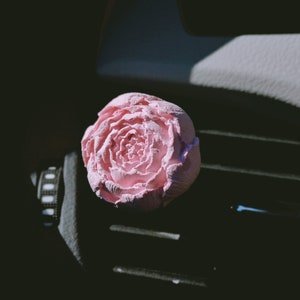 May include: A pink flower-shaped car air freshener. The air freshener is made of a soft, pliable material and has a realistic flower design.