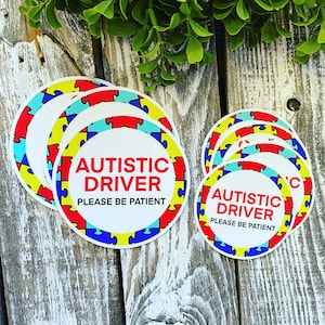 K&ouml;nnte beinhalten: Ein Satz von f&uuml;nf runden Aufklebern mit einem Muster aus blauen, gelben und roten Puzzle-Teilen. Die Aufkleber haben wei&szlig;en Text mit der Aufschrift "Autistic Driver Please Be Patient".