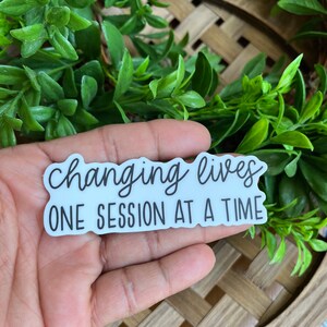 May include: White sticker with black text that reads "changing lives one session at a time".