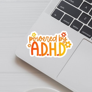 May include: Orange and yellow sticker with the text "powered by ADHD" with small flower and heart designs.