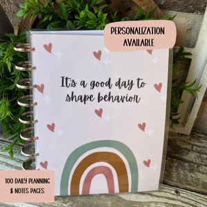 May include: A pink planner with a rainbow design and the text "It's a good day to shape behavior". The planner has 100 daily planning and notes pages. Personalization is available.