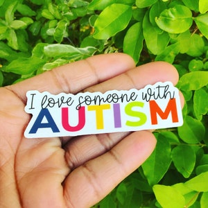 May include: A white sticker with the text "I love someone with AUTISM" in black. The word "AUTISM" is in rainbow colors.