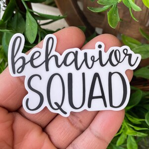 May include: White sticker with black text that reads "behavior squad".
