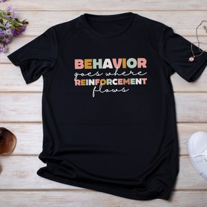 May include: Black t-shirt with the text "BEHAVIOR goes where REINFORCEMENT flows" in colorful letters.