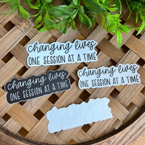 May include: Four stickers with the text "changing lives one session at a time" in black and white. Two stickers have a white background with black text, and two stickers have a black background with white text.