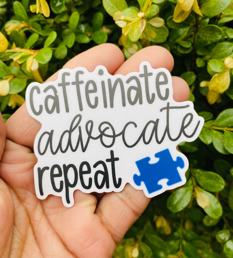 May include: White sticker with the text "caffeinate advocate repeat" in black cursive font. A blue puzzle piece is to the right of the text.