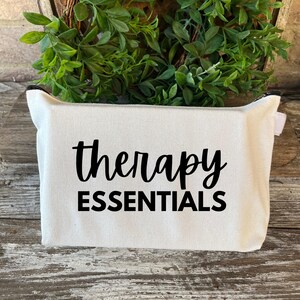 May include: White canvas zippered pouch with black text that reads "therapy essentials".