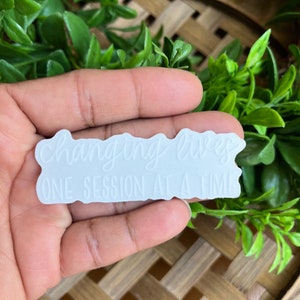 May include: White sticker with a wavy border that reads "changing lives one session at a time".
