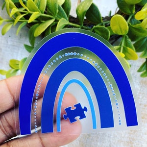 May include: A blue and white rainbow sticker with a blue puzzle piece in the center. The sticker is on a clear background.
