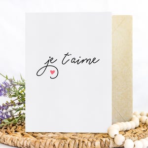 May include: A white card with the text "je t'aime" in black cursive script and a small pink heart.