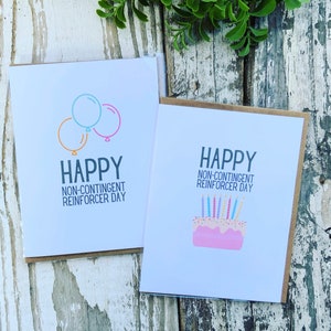 May include: Two greeting cards with the text "Happy Non-Contingent Reinforcer Day". One card features a cartoon image of three balloons. The other card features a cartoon image of a pink cake with candles.