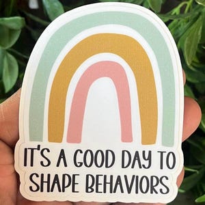 May include: A sticker with a rainbow design and the text "It's a good day to shape behaviors".