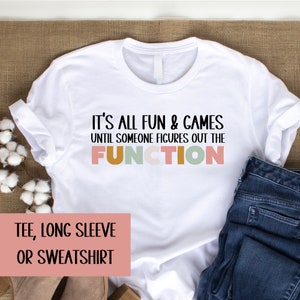 May include: White t-shirt with the text "It's all fun & games until someone figures out the FUNCTION" in black with the word "FUNCTION" in colorful letters.