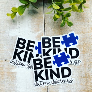 Puede incluir: Tres pegatinas blancas con texto negro que dice "Be Kind" y una pieza de rompecabezas azul. La pegatina de abajo tambi&eacute;n tiene el texto "Autism Awareness".