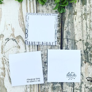 May include: Three white square notepads with black text on a rustic wooden surface. One notepad has the phrase "changing lives one session at a time." Another notepad has the word "data" with a line graph. The third notepad has a border of words.