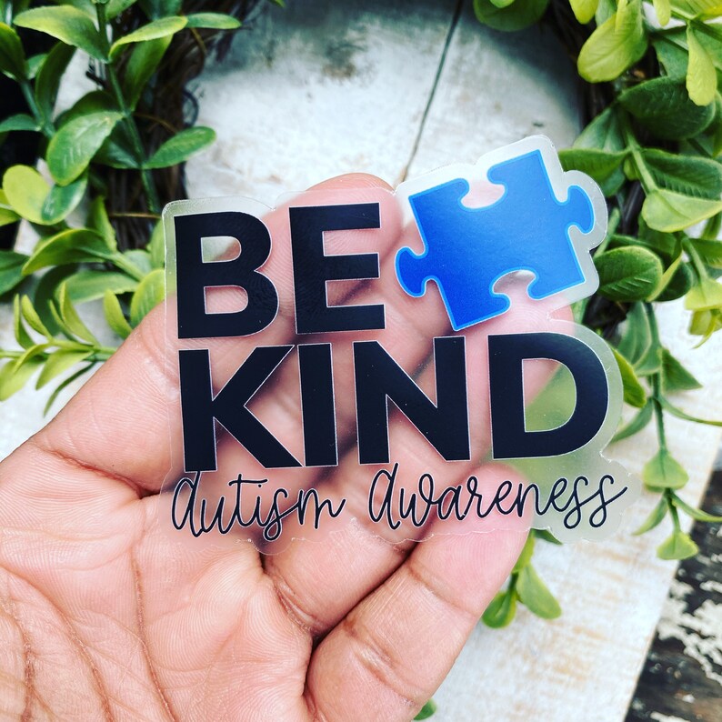 Puede incluir: Una pegatina transparente con las palabras "Be Kind" en texto negro y "Autism Awareness" en escritura cursiva. Una pieza de rompecabezas azul est&aacute; por encima de las palabras "Be Kind".