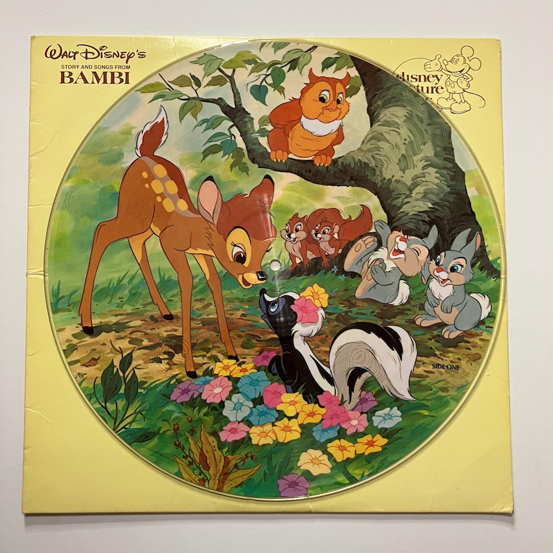 May include: A vintage vinyl record featuring characters from the Disney film "Bambi." The record's artwork showcases Bambi, a skunk, a rabbit, and other forest animals in a colorful, illustrated scene. The record is in a yellow sleeve.