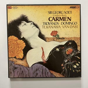 May include: A square vinyl record cover featuring an illustration of a person with dark hair lying down, wearing a black garment with floral patterns. The text reads: Sir Georg Solti Conducts Bizet's Carmen, Troyanos, Domingo, Te Kanawa, Van Dam.