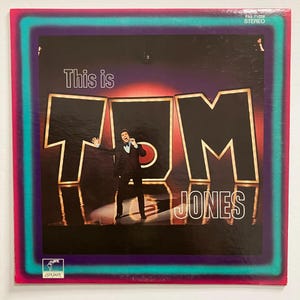 May include: A vintage vinyl record album cover featuring a photo of Tom Jones in a black suit and tie, standing in front of large red letters that spell out "TOM JONES". The album title is "This is TOM JONES" and the record label is "London".