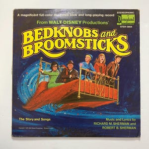 May include: Vintage "Bedknobs and Broomsticks" Disneyland record album cover. The cover features a colorful illustration of characters riding a bed through a starry night sky. Text includes "The Story and Songs" and "Music and Lyrics by Richard M. Sherman and Robert B. Sherman."