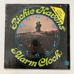 May include: A vinyl record album titled "Alarm Clock" by Richie Havens. The album cover features a clock design with a figure in the center. The text "HERE COMES THE SUN" is also visible. The album is sealed in plastic.
