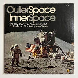 May include: A vintage record album cover featuring a black and white photo of an astronaut standing on the moon with a lunar module in the background. The album title is "Outer Space InnerSpace" and the text "The story of Jim Irwin, Apollo 15 Astronaut, and the Music of the Johnny Mann Singers" is printed below the title.