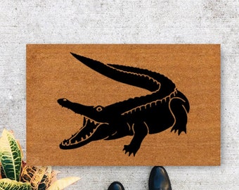 May include: A brown coir doormat with a black silhouette of an alligator with its mouth open.