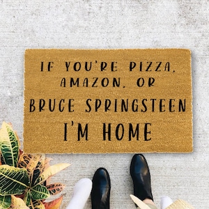 May include: A brown doormat with the text "If you're pizza, amazon, or Bruce Springsteen I'm home".
