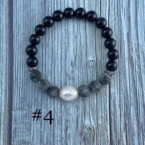 Puede incluir: Pulsera de cuentas negras y grises con una cuenta de perla blanca y detalles plateados. #4