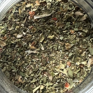 May include: A close-up view of a glass jar filled with a blend of dried herbs and spices. The mixture is a mix of green, brown, and red pieces, with a few small white specks.