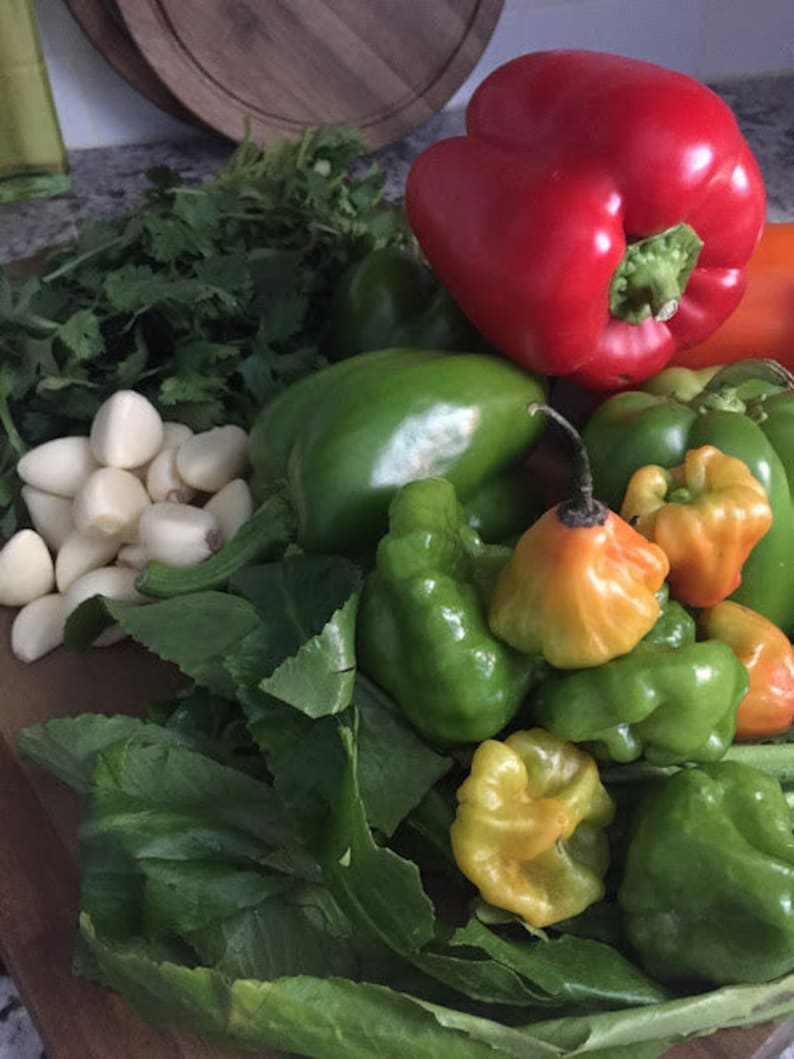 May include: A variety of green and red peppers, including bell peppers, habanero peppers, and jalapeno peppers, are arranged on a wooden cutting board with fresh cilantro and garlic cloves.