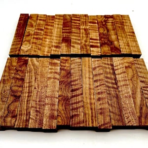 Puede incluir: Una colección de pequeños bloques de madera rectangulares. Los bloques están dispuestos en filas, mostrando un patrón de vetas de madera natural con tonos marrones y beige. La madera tiene una apariencia texturizada.