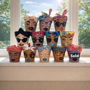 May include: A collection of hand-painted terracotta flower pots. Each pot features a unique face design with sunglasses or glasses, and a fabric head wrap. The pots are arranged on a windowsill with a bright, natural background.