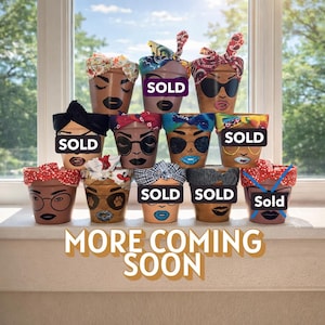 Puede incluir: Una colección de macetas de terracota pintadas, cada una adornada con un diseño de rostro único y una envoltura para la cabeza de tela. Las macetas presentan varios tonos de piel, expresiones faciales y cintas para la cabeza coloridas. Se muestra el texto "MORE COMING SOON".