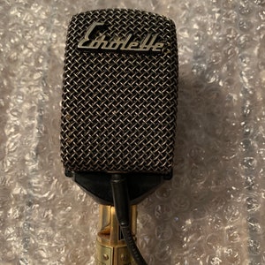 May include: A black microphone with a silver grille and the word "Schoeps" printed on it. The microphone has a gold-colored base and a black cable.