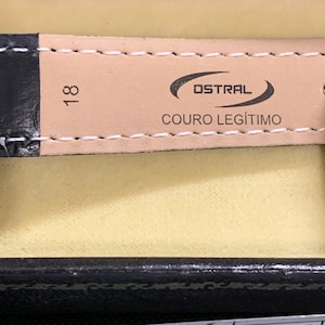 Op de afbeelding: Een close-up van een bruin leren horlogebandje met de tekst "OSTRAL COURO LEG&Iacute;TIMO" en het nummer "18" erop gedrukt.