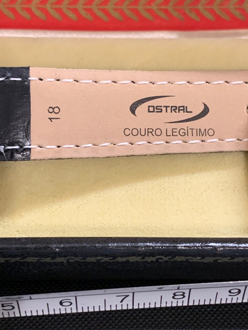 Op de afbeelding: Een close-up van een bruin leren horlogebandje met de tekst "OSTRAL COURO LEG&Iacute;TIMO" en het nummer "18" erop gedrukt.