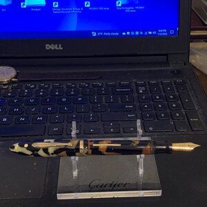May include: A black, gold, and white patterned fountain pen with a gold nib resting on a black and white stand with the word "Cartier" printed on it.