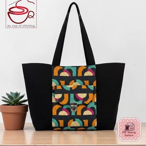 May include: Black tote bag with a colorful geometric pattern on the front pocket. The pattern includes orange, teal, and pink semi-circles on a black background. The bag has long black handles and a silver clasp. The text "my cup of stitching" is visible.