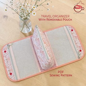 Peut inclure: Un organisateur de voyage avec pochette amovible au motif floral dans des tons rose et blanc. L'organisateur comprend des poches en filet, des fermetures éclair argentées et un bord corail. Texte : TRAVEL ORGANIZER WITH REMOVABLE POUCH et PDF SEWING PATTERN.