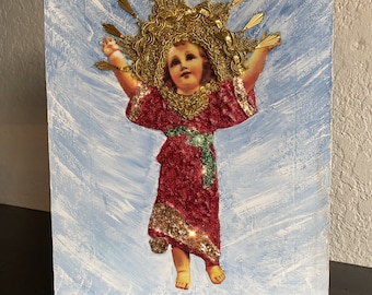 May include: A painting of a child in a red dress with gold glitter and a gold crown. The child is surrounded by a blue background with white brushstrokes.