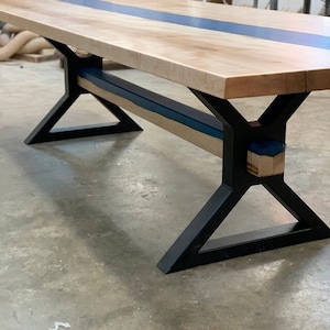 May include: A wooden table with a blue epoxy resin inlay and black metal legs. The table has a modern design and is perfect for a dining room or kitchen.