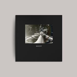 May include: A black square wedding album with a vintage photograph of a couple embracing near a fountain. The photograph is in black and white. The Roman numeral "MMXXV" is printed at the bottom of the album.